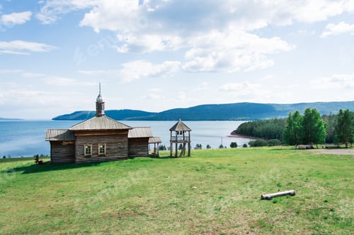 Preview: An old wooden Russian house with a bell tower on the river bank on a summer day