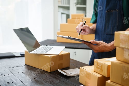 Preview: A man is working at his desk, preparing parcel boxes for shipment. He checks packs items carefully