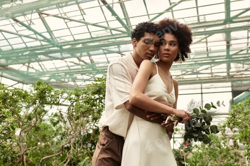 Preview: Young couple shares a tender moment surrounded by vibrant greenery and blooming plants