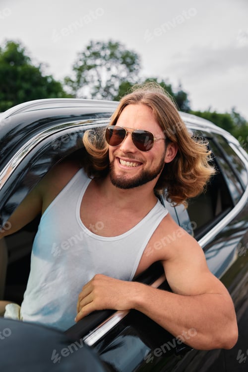Preview: Man in sunglasses smiling from car window with a nature background