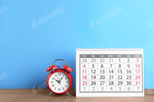 Preview: Calendar and alarm clock on wooden table against light blue background