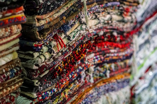 Preview: Closeup of colorful ethnic rugs stacked on each other at an outdoor shop with a blurry background