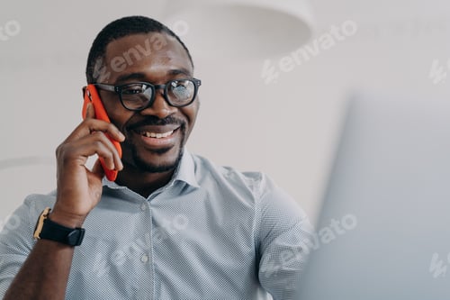 Preview: Happy african american businessperson in glasses hold phone makes business call in front of laptop