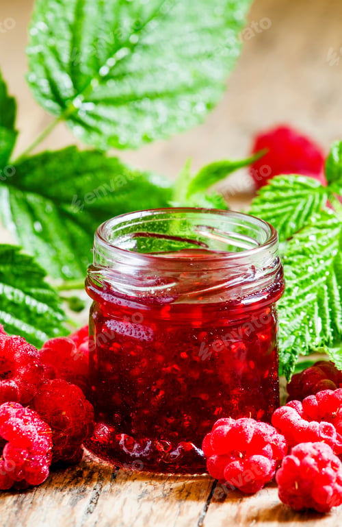 Preview: Raspberry jam with fresh raspberries and green leaves on the old wooden background, selective focus