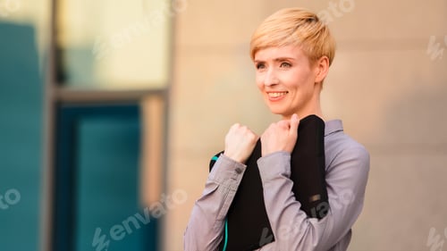 Preview: Happy mature adult business woman boss leader stands outdoors near company office building holds