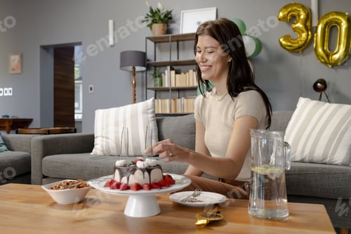 Preview: Woman celebrating birthday at home, smiling while cutting cake on table