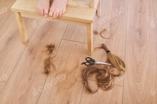 Preview: Trimmed hair of child girl and scissors on the floor at home