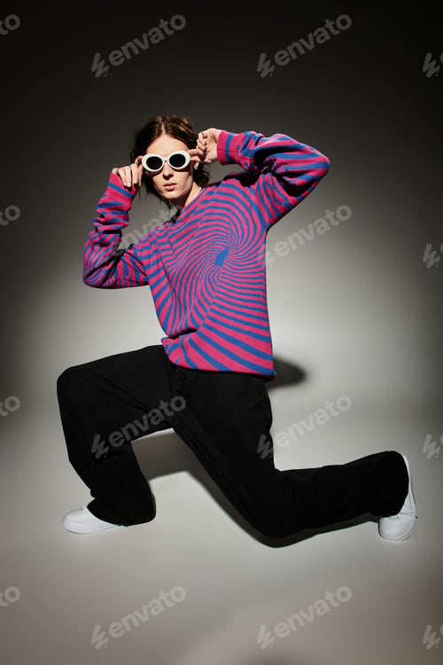 Preview: Handsome young man poses confidently, showcasing a unique colorful sweater and trendy sunglasses.