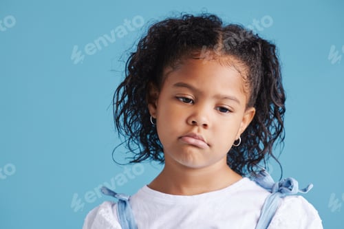Preview: Offended little hispanic girl looking sad and upset while posing against a blue studio background.