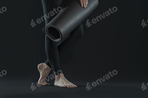 Preview: Young woman legs practicing yoga and yoga mat on a dark black background. copy space