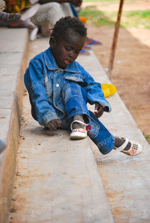 Preview: Little black girl in jeans sitting in the steps playing