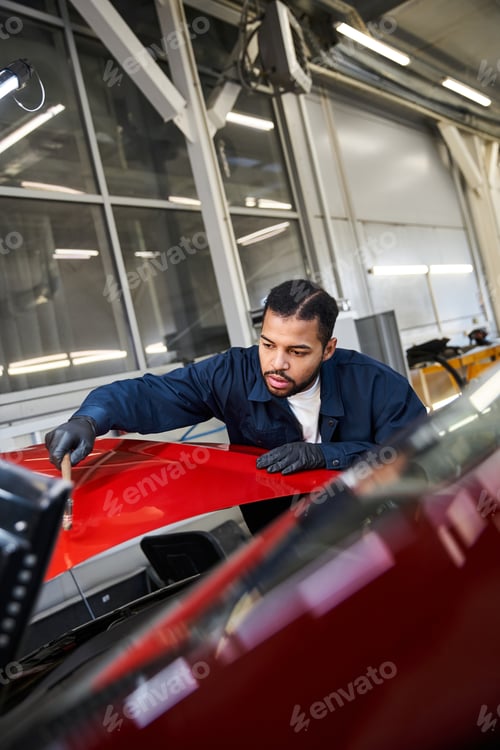 Preview: Handsome young mechanic diligently working on a car in a modern workshop at midday