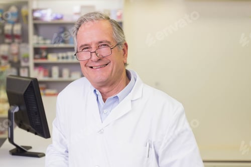 Preview: Senior male pharmacist in lab coat standing behind counter at pharmacy using computer monitor