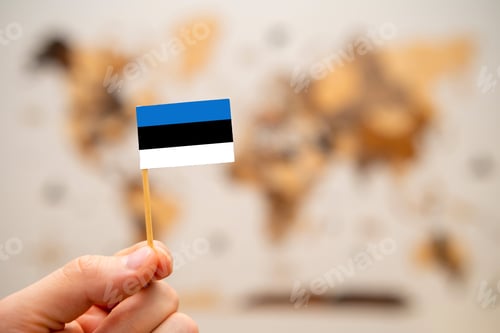 Preview: Estonia flag in mans hand on the world map background.