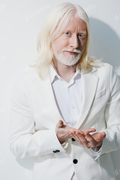 Preview: Portrait of a man with long white hair wearing a white suit, standing against a plain white