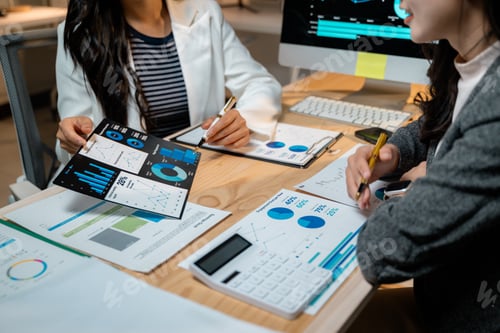 Preview: Businesswomen analyzing financial charts and graphs at office desk