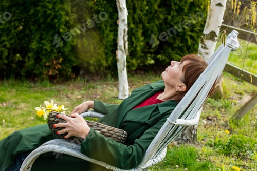 Preview: Senior woman sits in armchair in spring time garden
