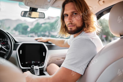 Preview: Man with long hair seated in a car looking at the camera, relaxed expression, interior showcasing