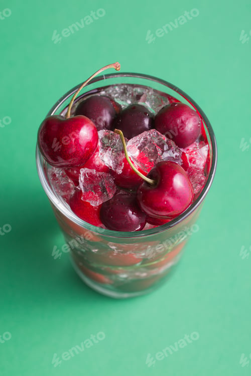 Preview: Cherries in a glass with ice on green background
