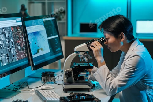 Preview: Asian female scientist looking in microscope during investigation