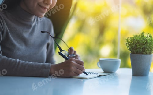 Preview: Closeup image of a beautiful young asian woman writing on a blank notebook on the table