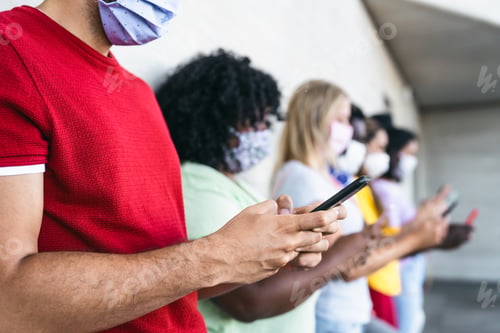 Preview: Young people wearing face mask using mobile smartphone outdoor