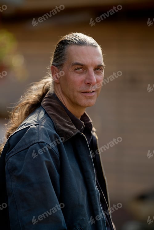 Preview: Man with long hair and denim jacket standing outdoors with blurred background. Brandenburg, Germany
