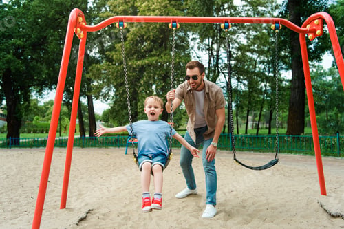 Preview: father and son having fun on swing at playground in park