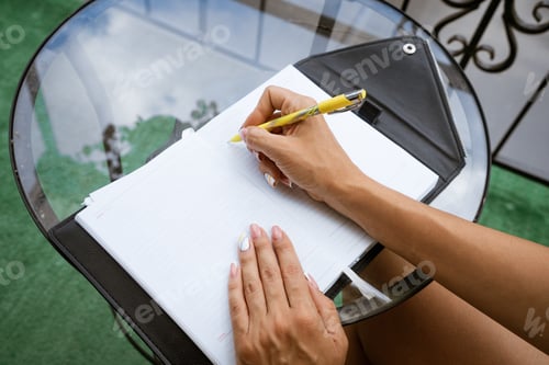 Preview: woman writes in a notebook at a table on the terrace