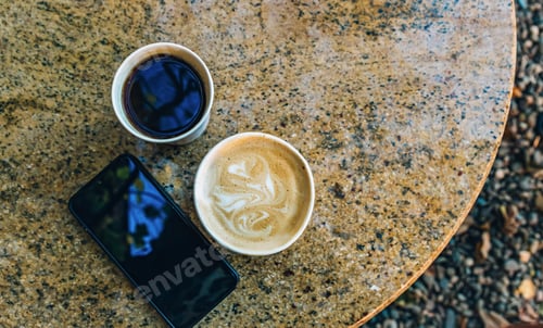 Preview: Two paper coffee cups with americano and cappuccino on a stone table at an outdoor cafe.