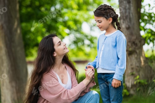 Preview: joyful woman holding hand of daughter in park