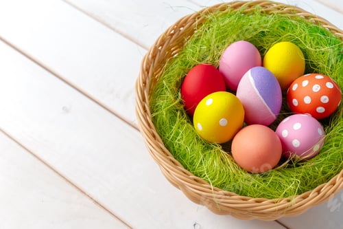 Preview: Colorful eggs in a woven basket surrounded by green grass on a wooden surface
