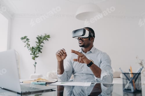 Preview: African american businessman use virtual reality glasses working at laptop at office desk. High-tech