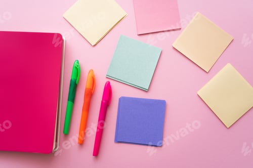 Preview: top view of colorful pens near bright notebook and blank paper notes on pink