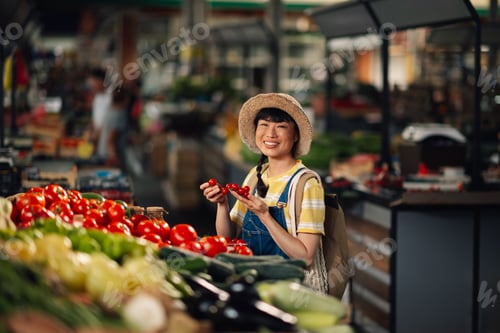 Preview: Asian woman at market smiling holding small tomatoes, fresh vegetables