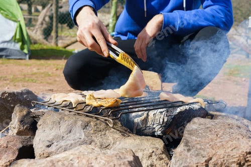 Preview: Unrecognizable man sitting by wood fire cooking. Camping concept
