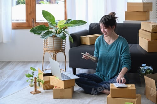 Preview: Young asian woman using calculator and preparing products for deliver to customers.