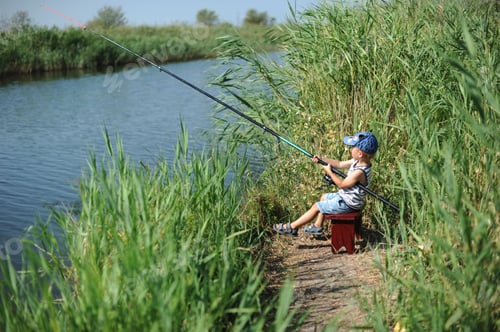 Preview: Little cute boy sitting on a little bench, holding big rod and fishing in the river with high grass