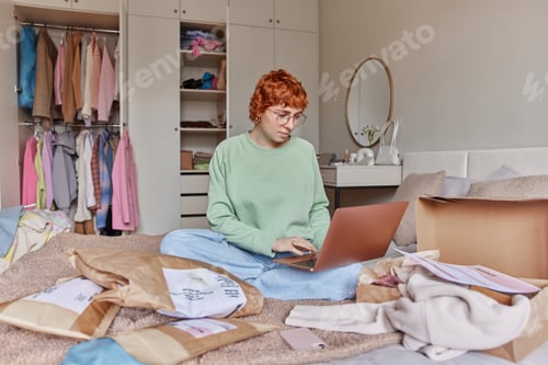 Preview: Serious red head woman uses laptop for selling clothes online makes order prepares parcels for
