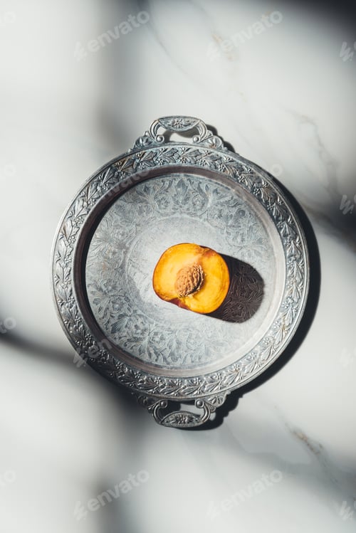 Preview: top view of piece of peach on metal tray on light marble tabletop with shadows