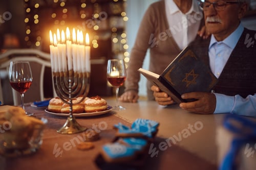 Preview: Close up of senior couple reading Tanakh while celebrating Hanukkah at home.