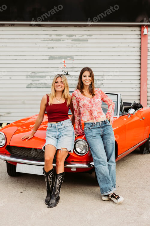 Preview: Two young women leaning on a red convertible car enjoying travel adventure