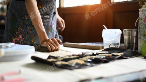 Preview: Pottery artist in apron kneading piece of raw clay on wooden table.
