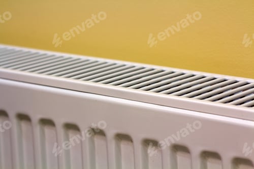 Preview: Close-up of white heating radiator detail on light yellow wall copy space background.
