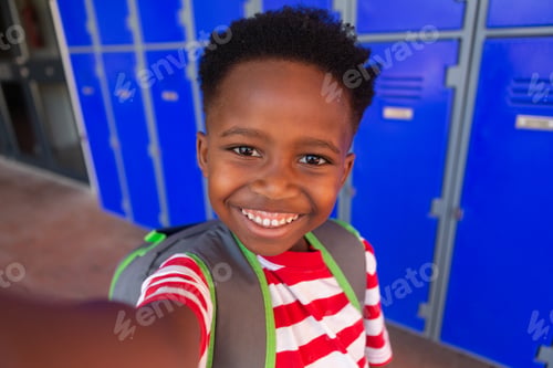 Preview: Front view of a happy African American schoolboy standing in the corridor at school