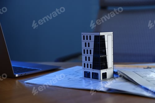 Preview: Real estate. Apartment building model, architectural drawings and laptop on table indoors, closeup