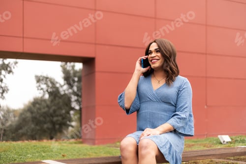 Preview: Trans woman sat in modern outdoors talking in cellphone