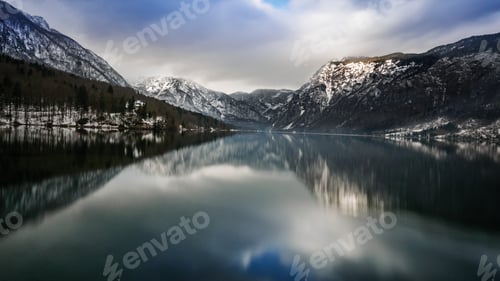 Preview: Moody sky over a lake in mountains. Winter landscape with reflection of mountains in water.