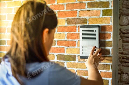Preview: Close up of woman using intercom at building entrance.