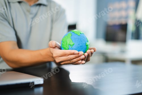 Preview: Young man holding earth model and phone in office, symbolizing green tech, global connection,